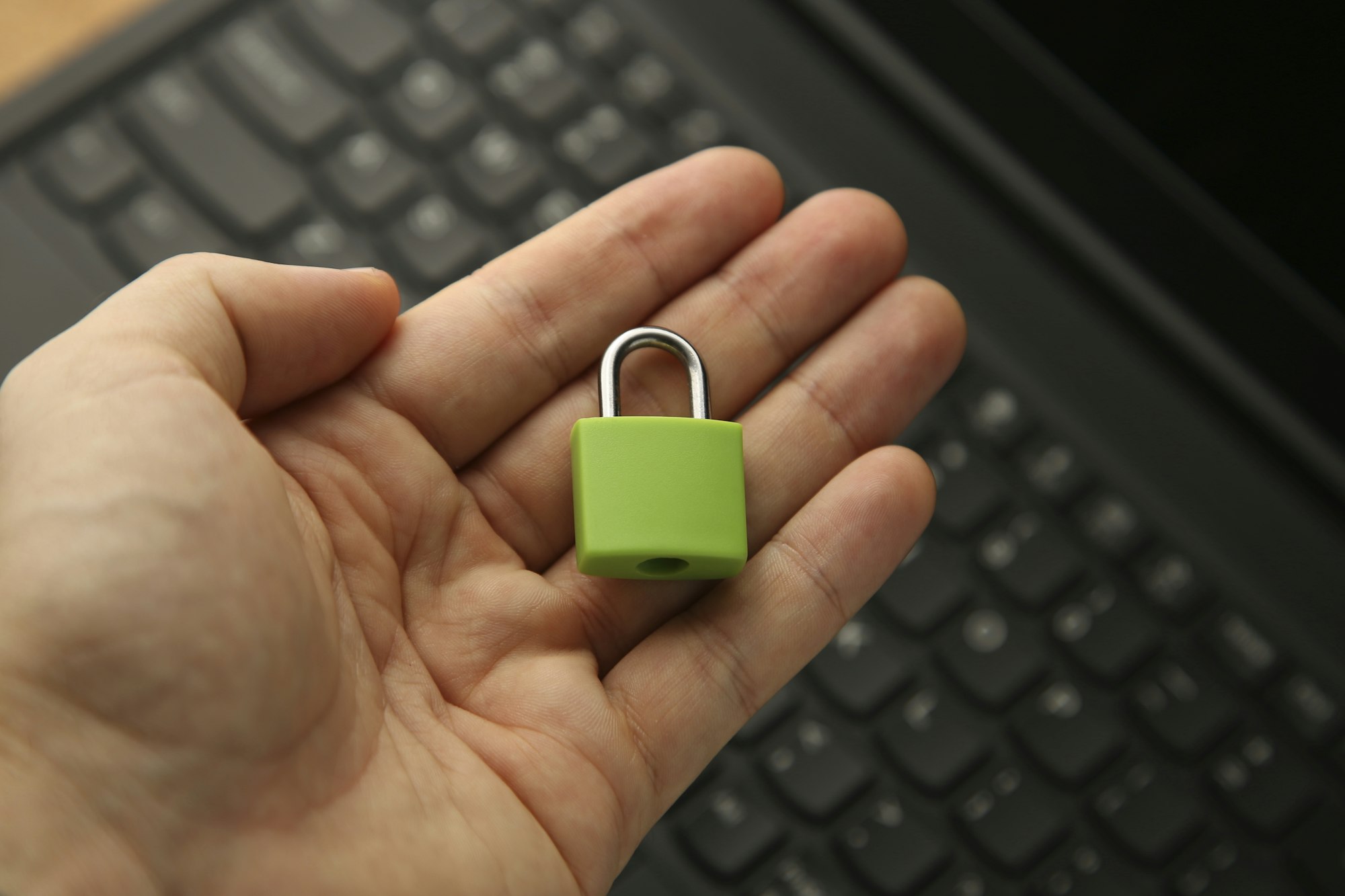 A hand holding a green padlock with a laptop in background. Cyber security concept.